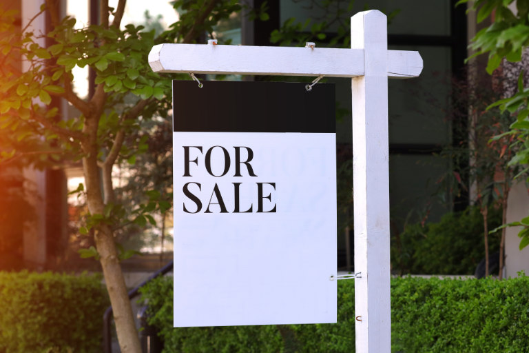 A white ‘For Sale’ sign sits outside a building.