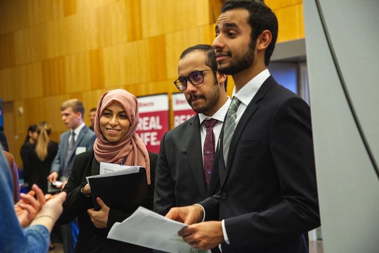 Three students smile and speak with employers at the Kelley Career Fair.